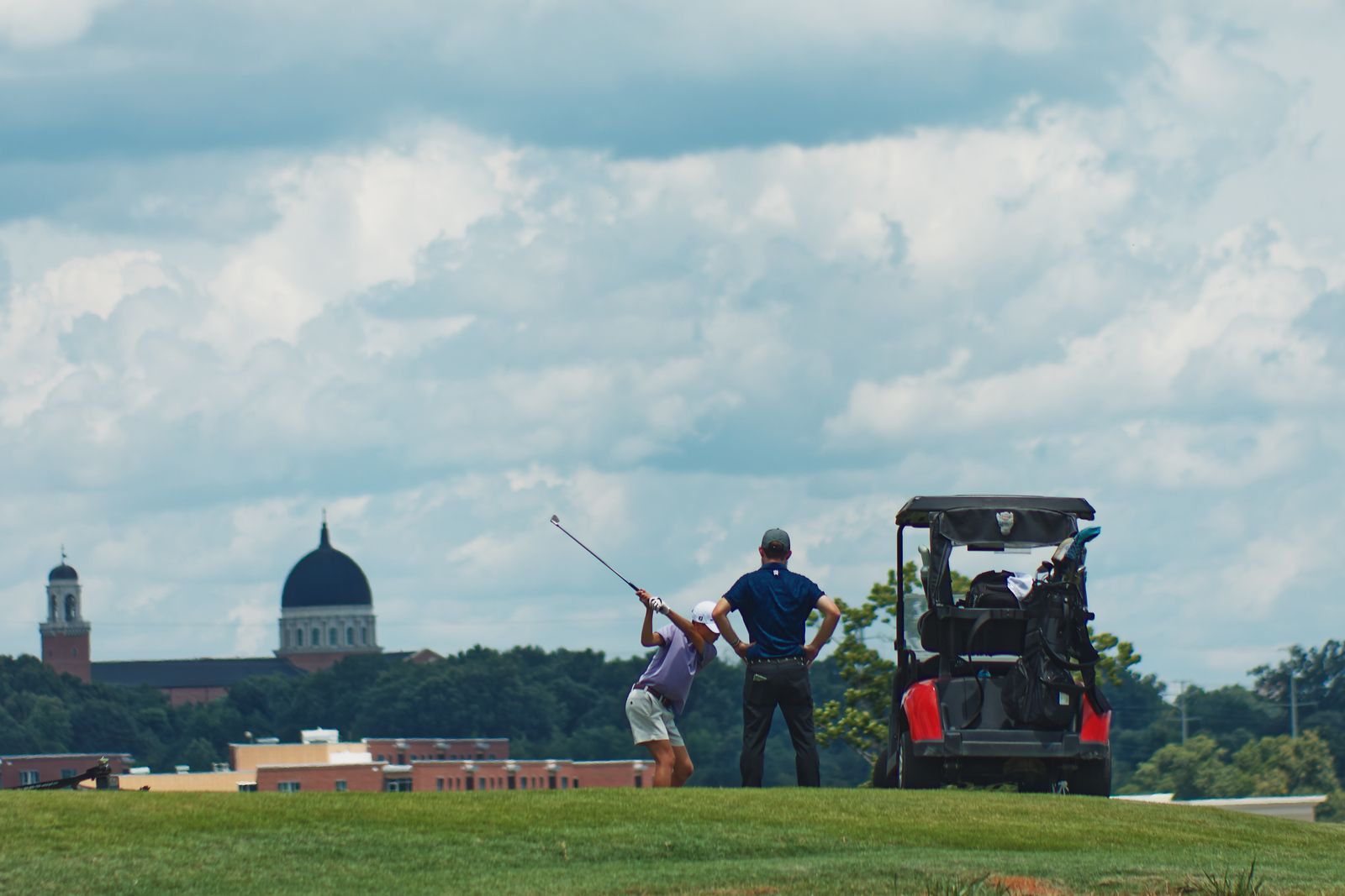 A golf caddie observes a player swinging a club